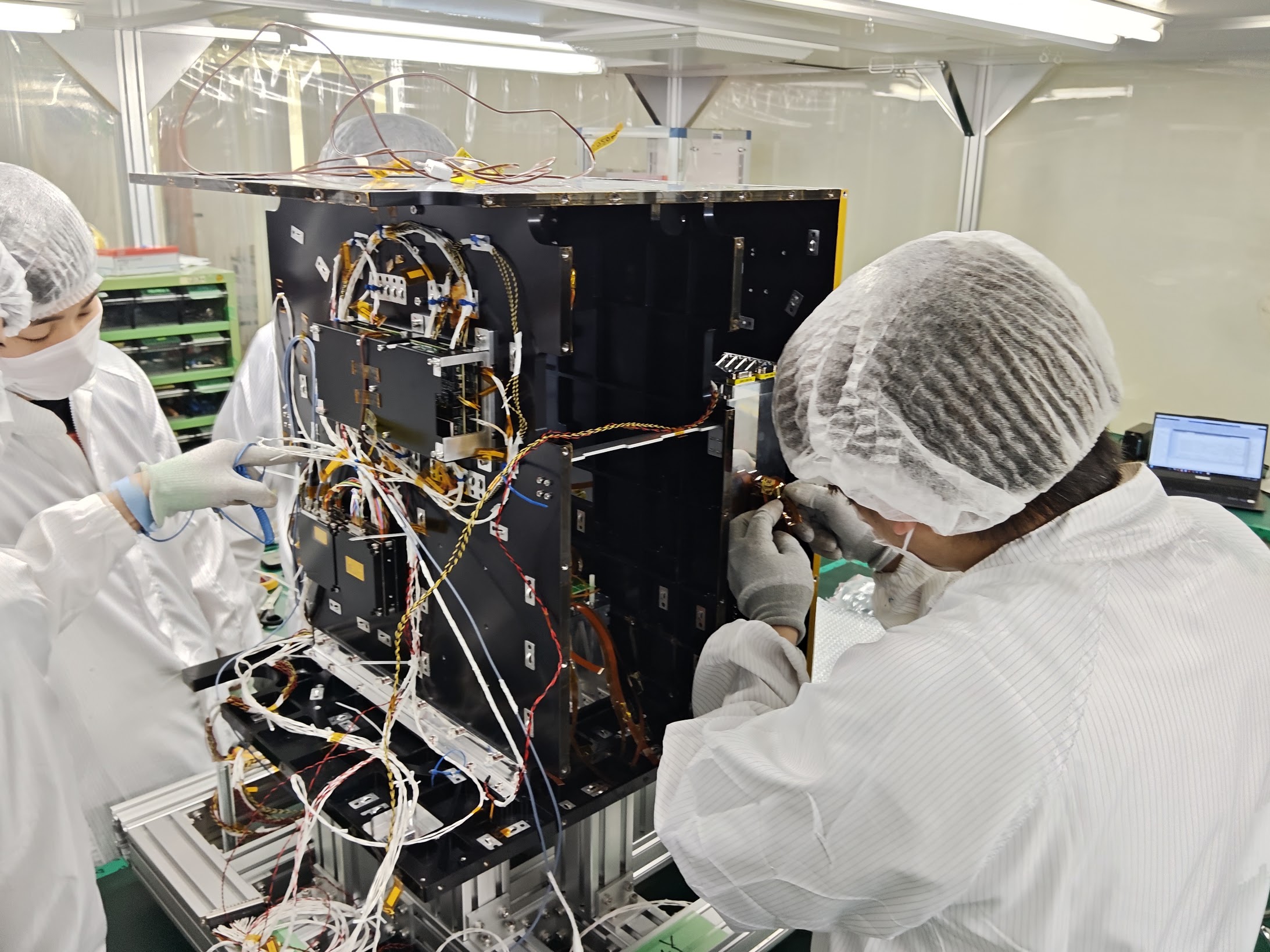 クリーンルームで防塵服を着て小型衛星の組み立て・配線作業を行う様子